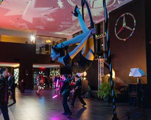 Aerial performers in blue costumes dance suspended from silk ribbons at an indoor Mercedes-Benz event with colorful lighting.