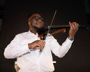 A violinist in a white dress shirt performs passionately against a dark background.