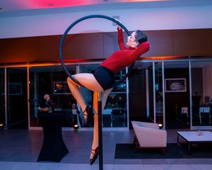Dancer performs graceful aerial moves with red fabric in dimly lit studio space.
