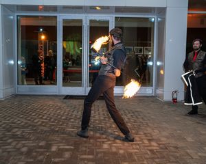 Fire performer spinning flaming batons in an outdoor courtyard at night creating dramatic light trails.