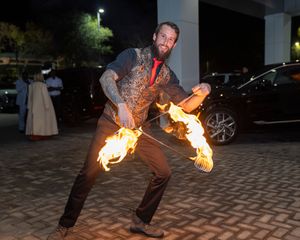 Fire performer spinning flaming torches in dramatic sequence against dark background at night.
