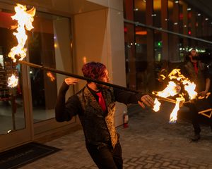 Fire dancers performing with flaming props in an indoor venue with dramatic lighting.