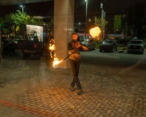 Fire artist performs a dynamic fire spinning routine on a paved courtyard at night.
