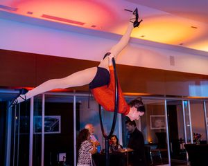 Acrobatic pole dancer performs horizontal split pose during indoor entertainment show.