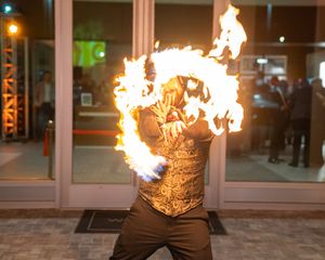 Fire performer in gold vest creates dramatic flame display against dark storefront.
