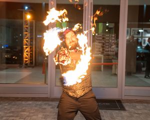 Fire performer executing dramatic flame display in front of glass building entrance.