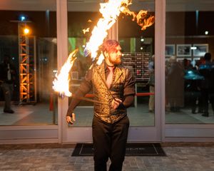 Fire performer executes dramatic moves with flaming props in front of a modern building facade.