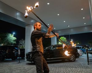 Fire performer spinning flaming batons in a dark outdoor space.