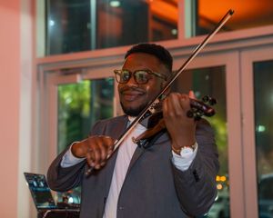 Musicians perform with violins in an elegant venue with warm lighting and glass windows.