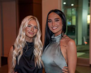 Two women in elegant evening attire pose together at an indoor event.