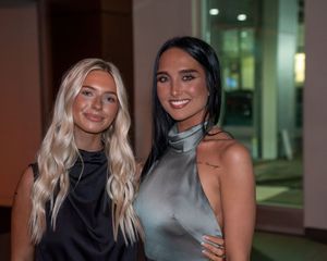 Two women in elegant evening wear posing together at nighttime event.