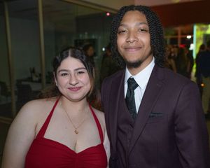 A group poses together at a formal event wearing elegant attire including red dresses and dark suits.