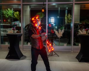 A fire performer twirls flaming batons in front of a building at night creating dramatic light trails.