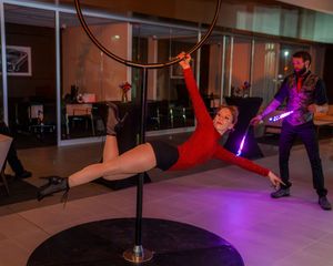 Aerial performers practicing on hoops in a dimly lit studio with purple lighting effects.