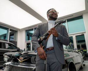 Business professional in formal attire reviews paperwork while standing next to vehicles outdoors.