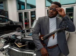 Professional wearing gray suit examines luxury car details in modern showroom setting.