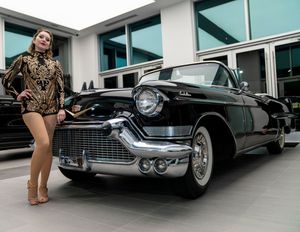 Classic vintage Cadillac cars displayed outside a modern building with glass facade.