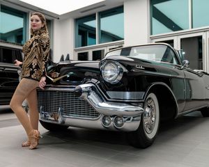 Vintage black Cadillac displayed at modern building with retro-styled performers posing.