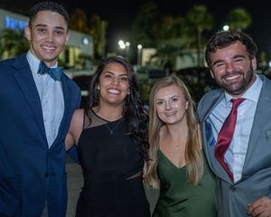 Formal event attendees in evening wear pose together outdoors at night.