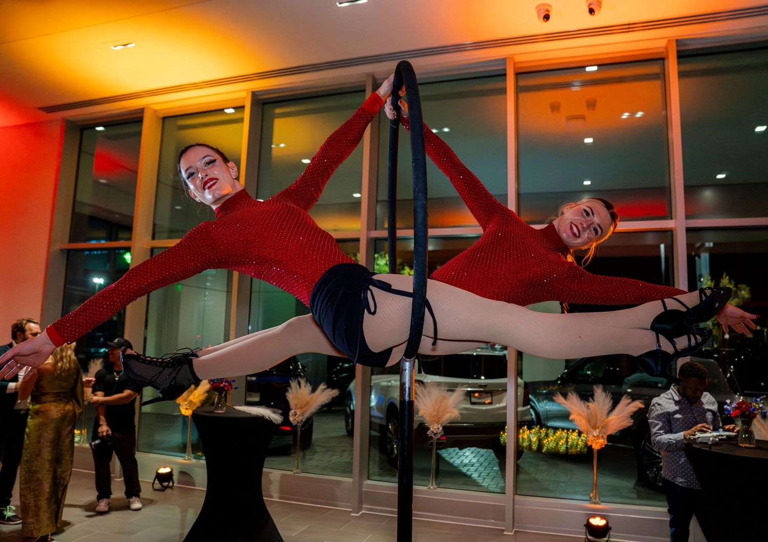 Two performers in red costumes demonstrate synchronized aerial acrobatics on suspended apparatus.