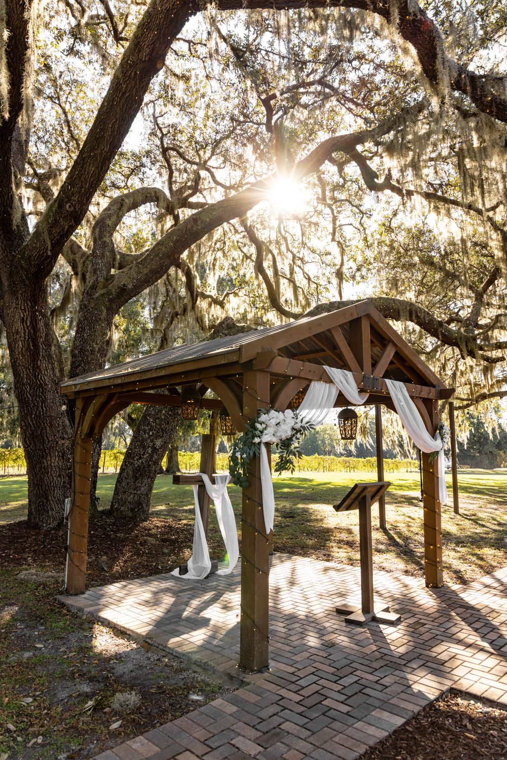 A rustic wooden pavilion with Spanish moss hanging from oak trees creates a romantic wedding ceremony setting.
