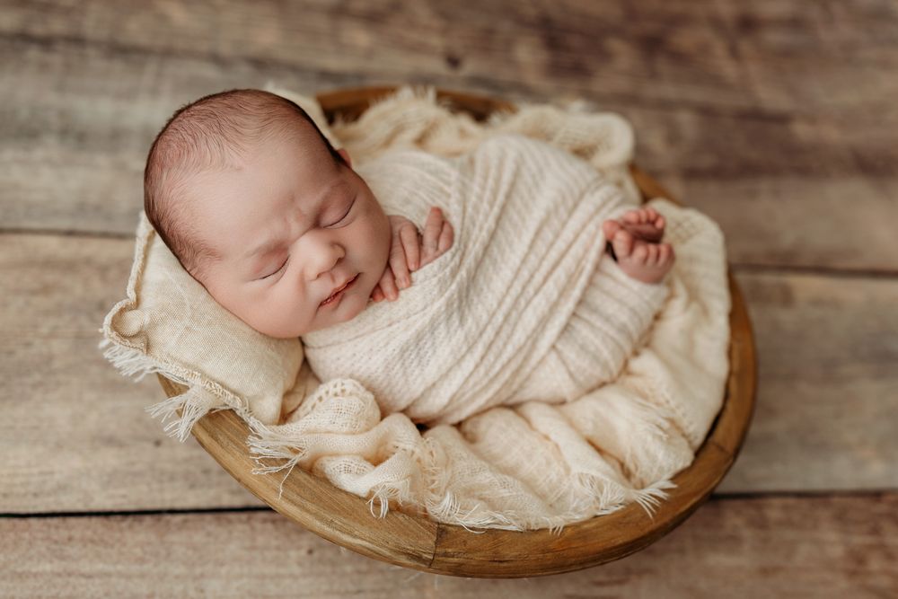 A sleeping baby swaddled in cream colored fabric lying on rustic wooden surfaces in a series of photos.