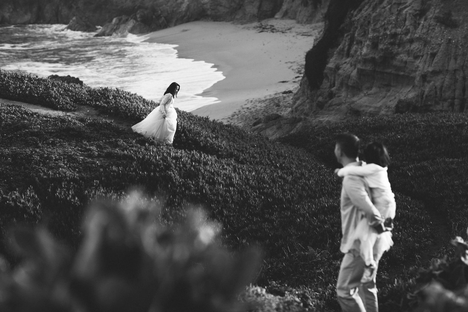 Bride and groom walking along a dramatic coastal cliff at sunset, their intimate elopement framed by crashing waves in Half moon Bay