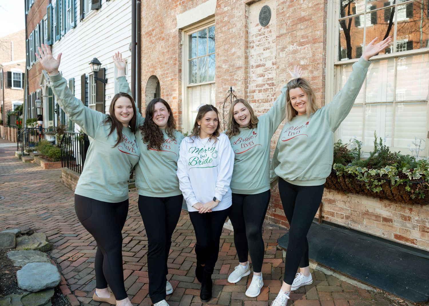 Bride surrounded by bridesmaids wearing matching sweatshirts — candid wedding celebration portrait