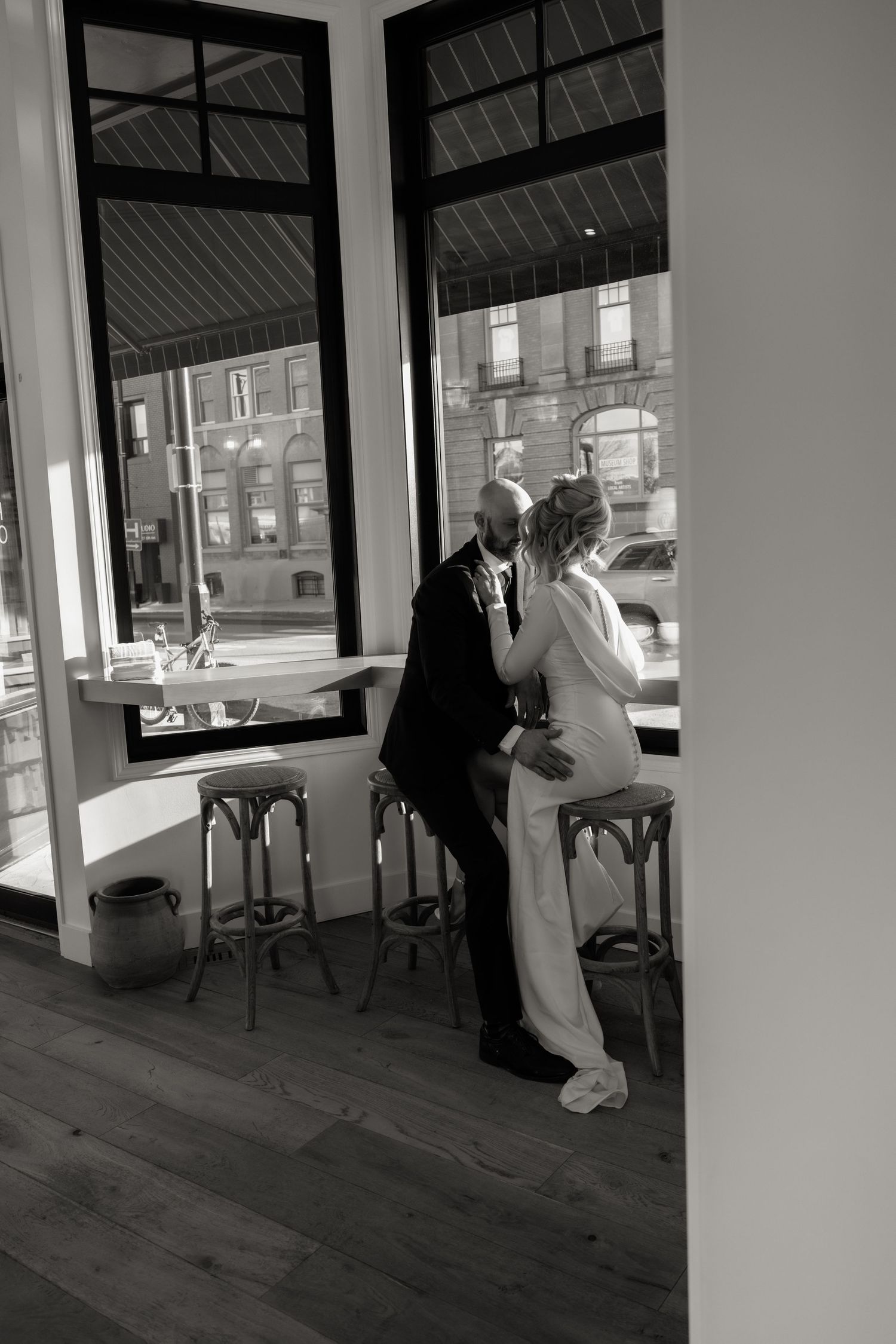 Two figures in white protective suits and masks inspect a room with large windows and hardwood floors.