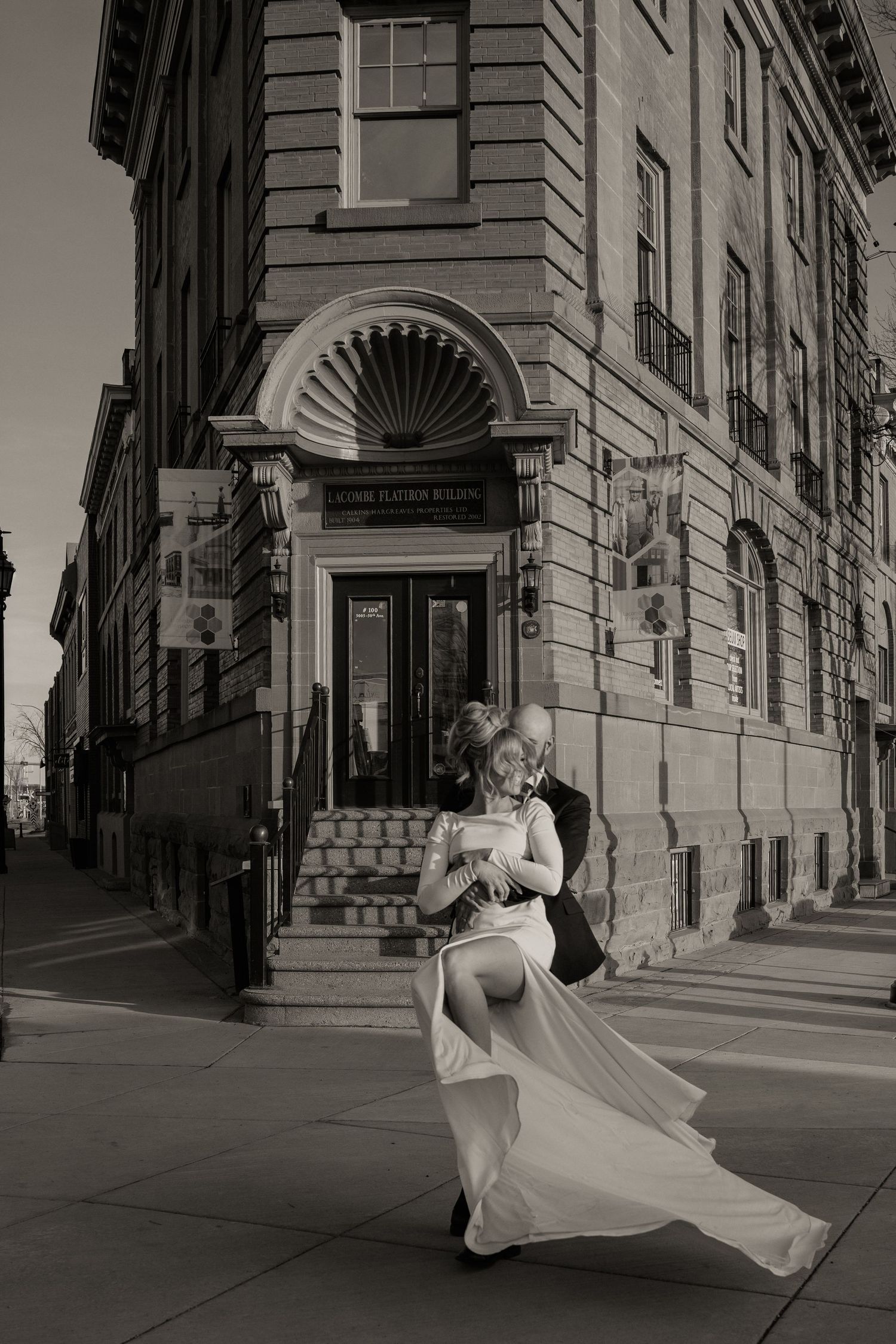 A black and white photo series shows a person in a flowing white dress twirling through an urban street with classic architecture.