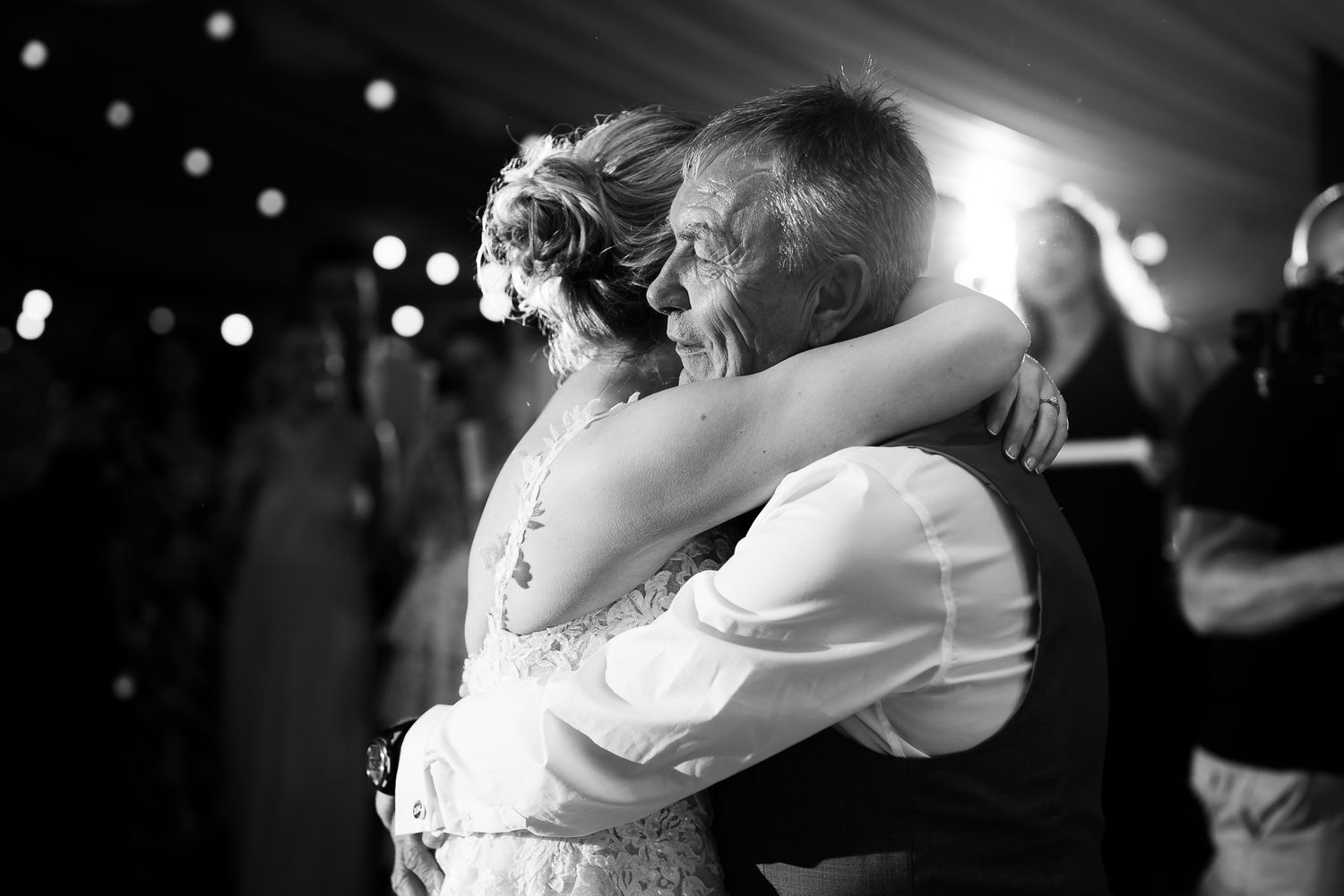 A couple shares an intimate dance together at a wedding reception with string lights twinkling in the background.