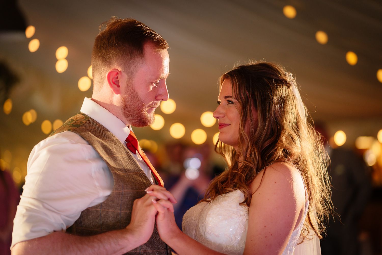 A couple shares a romantic dance together under warm glowing lights at their wedding reception.