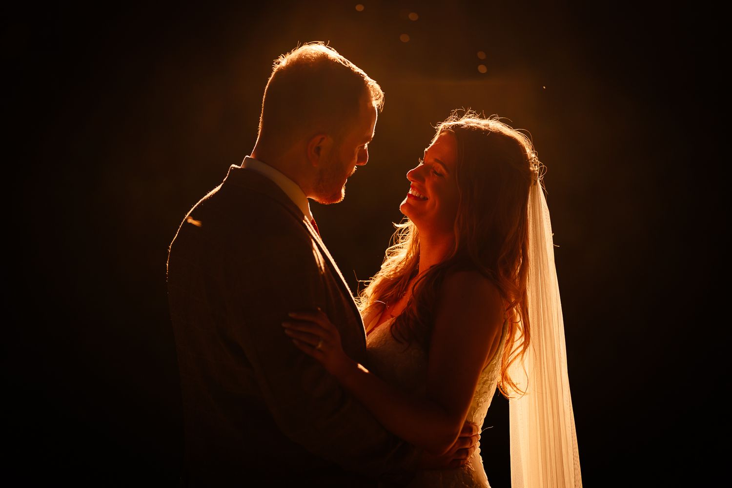 A silhouetted couple shares an intimate moment in dramatic backlit wedding photography.