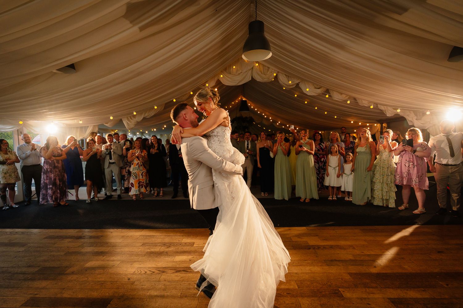 A couple dances together during their first dance at a wedding reception under a tent with string lights.