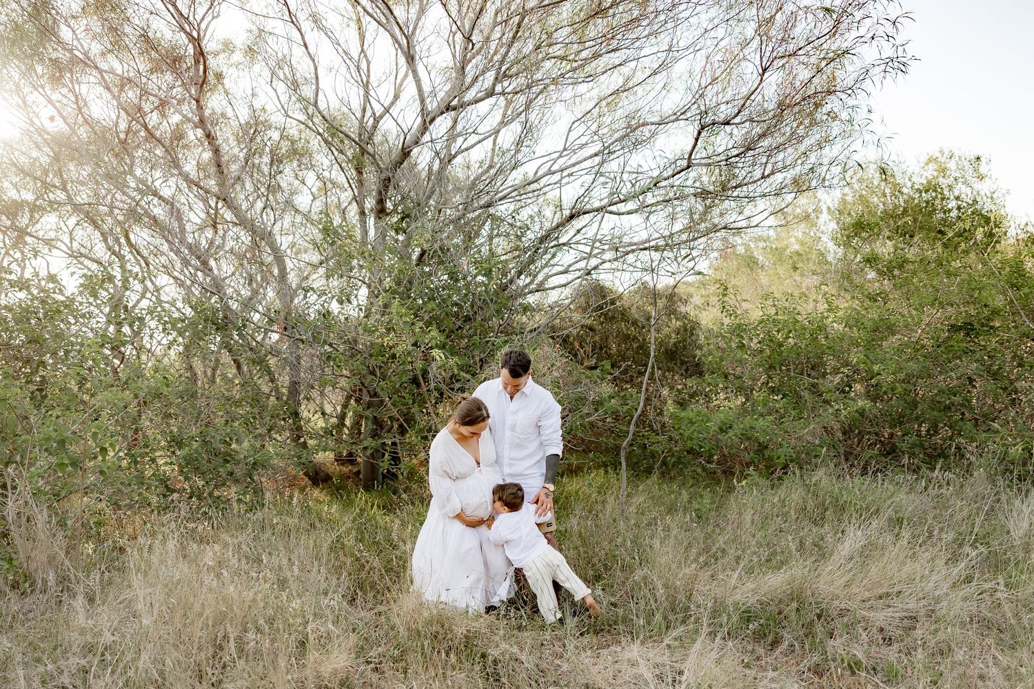 White-clothed figures sitting among natural brush and trees in an outdoor setting.
