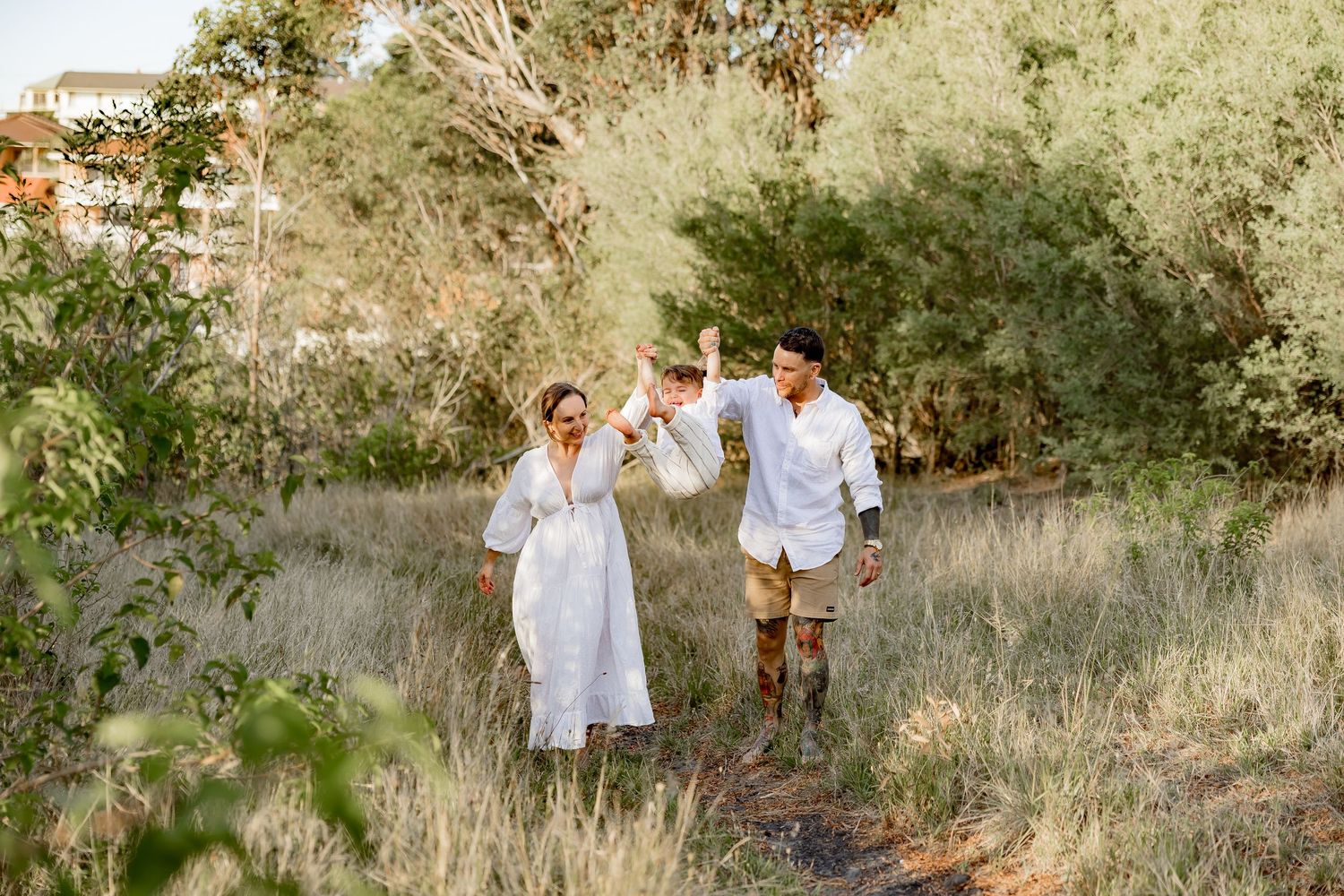 Family in white clothing poses together on grassy hillside during golden hour.