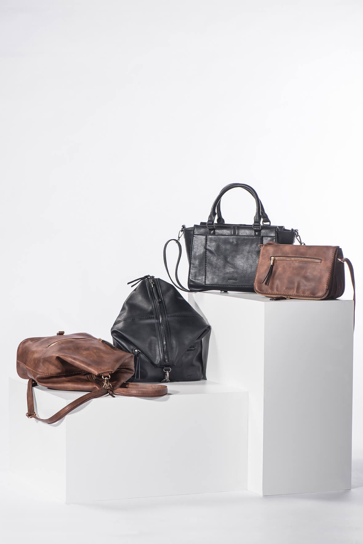 Stylish leather duffle bags and handbags in black and brown arranged on white display blocks.  Montreal, Canada, product Photography.