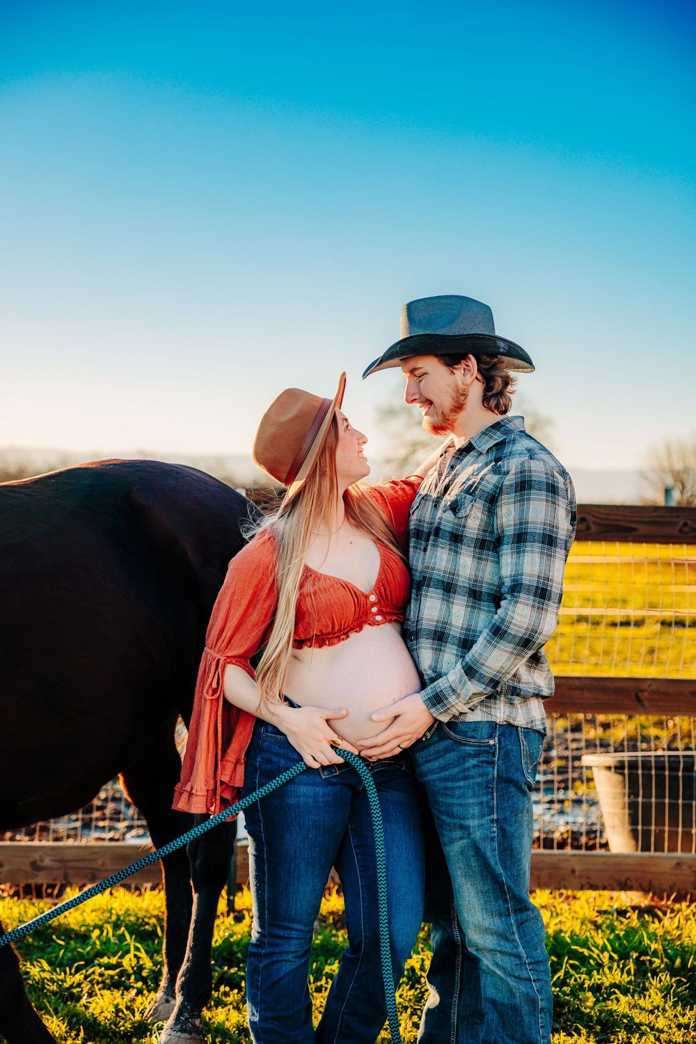 A couple shares an intimate moment beside their horse in a sunlit pasture during golden hour.