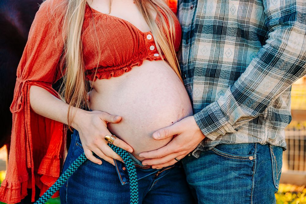 A couple in plaid and red embraces while showing their engagement ring in a romantic outdoor setting.