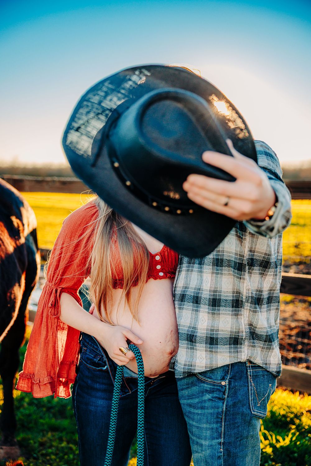 Couple in western attire sharing intimate moments at sunset in a field.