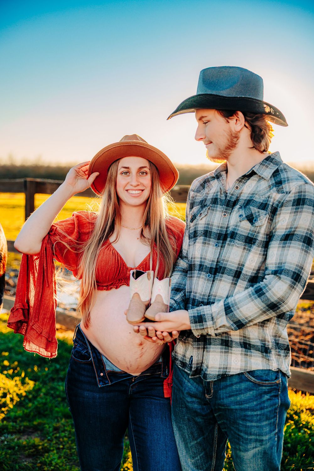 A couple wearing western attire poses together in a field during sunset with vibrant yellow wildflowers.