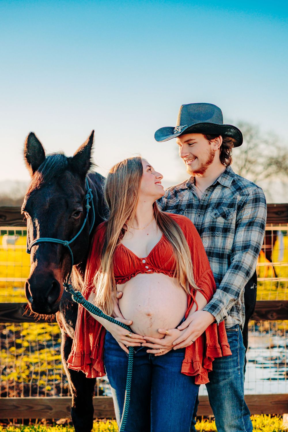 A maternity photoshoot featuring a couple with their black horse on a ranch during golden hour.