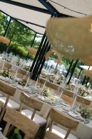 Elegant wedding reception setup with rustic wooden tables and white chairs under a tent.
