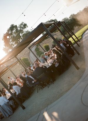 Wedding guests enjoying an outdoor celebration at sunset with string lights overhead.