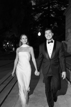 Elegant couple walking together at night in formal black tie attire.