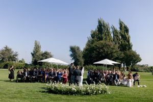Outdoor wedding ceremony with guests seated under tall poplar trees.