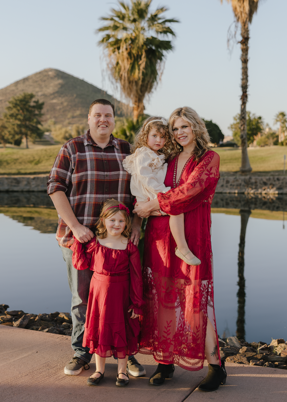 A family of four poses by a reflective pond with a mountain backdrop in warm golden light.