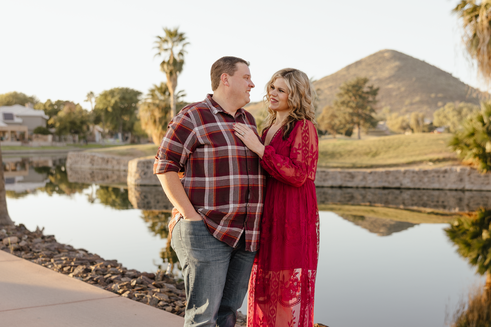Couple sharing a romantic moment by a pond with palm trees and a mountain in the background at golden hour.