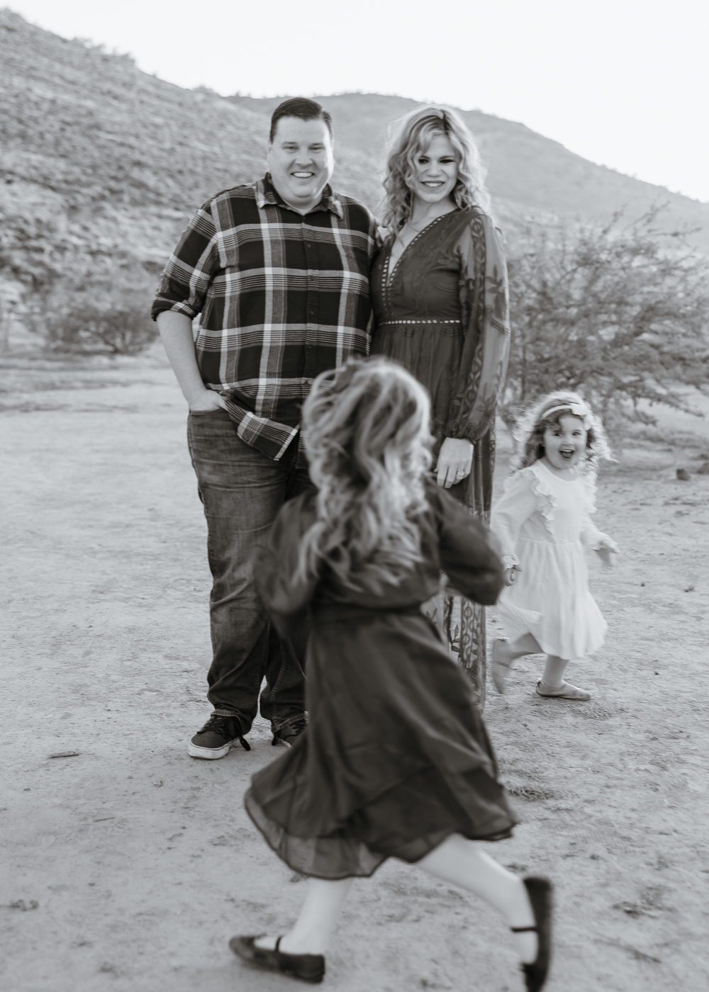 Black and white photo of a couple watching their two young daughters play in a scenic desert landscape.