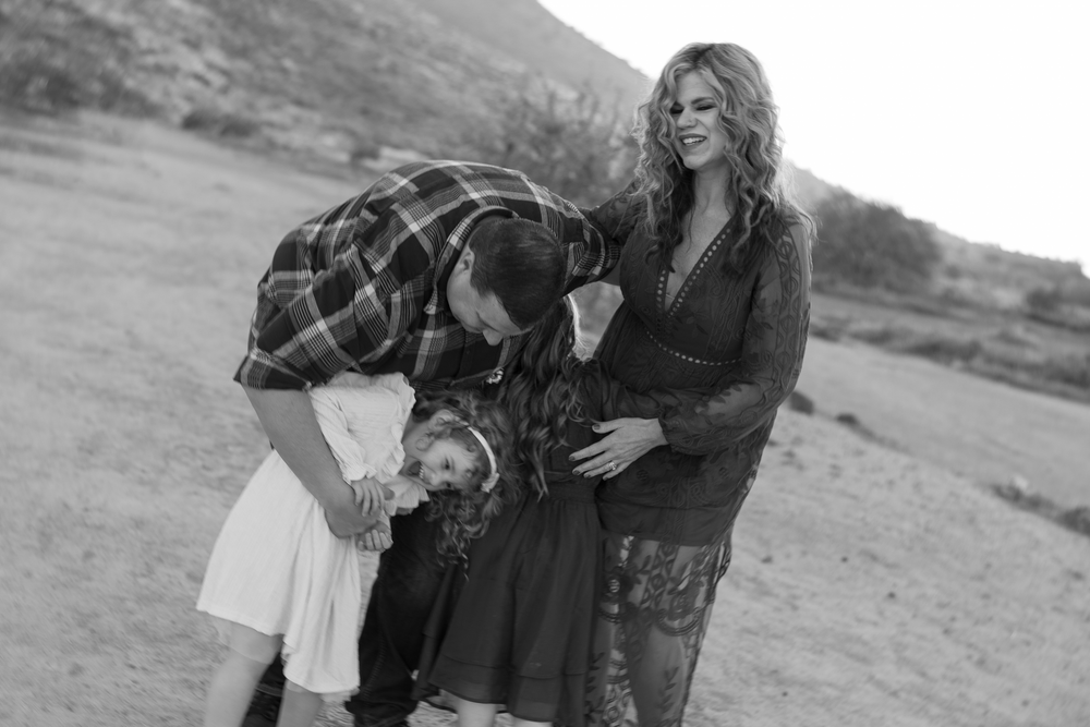 Black and white photo of a couple with a small dog and child in a desert setting at dusk.